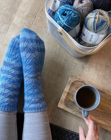 blau gestreifte Socke mit Strukturmuster, Tasse Tee und ein Korb voll Wolle